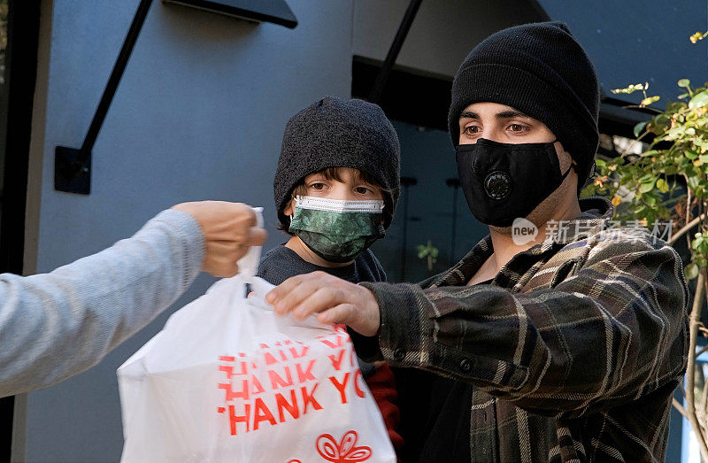 一名失业的年轻人带着他的儿子，戴着防护口罩从慈善中心领取免费餐食
