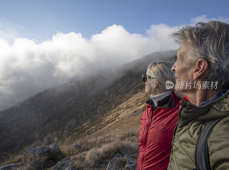 一对成熟的夫妇早晨沿着长满草的山坡徒步旅行