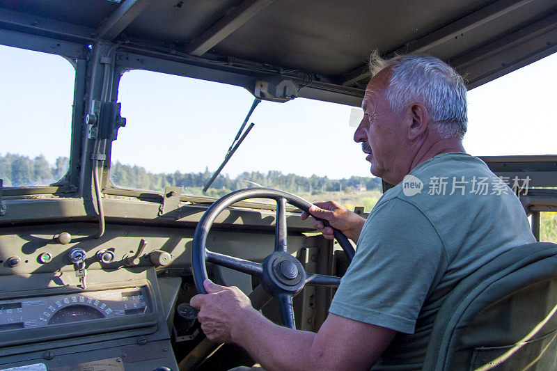 一个白发男子开着一辆很旧的军用车辆。作战中的军用车辆。重建生活和作战行动。军事