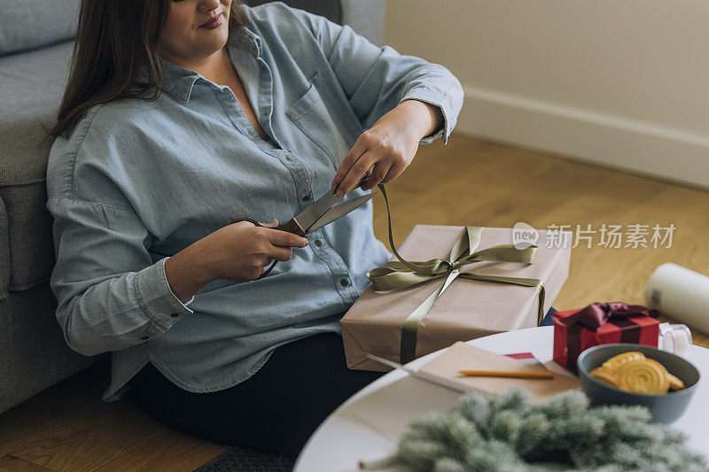 匿名的大号女人在包装礼物时剪掉多余的丝带