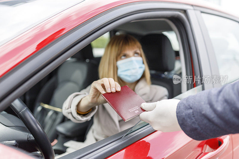 一名女子驾驶着一辆带着防护面罩的汽车，将护照交给边防警察