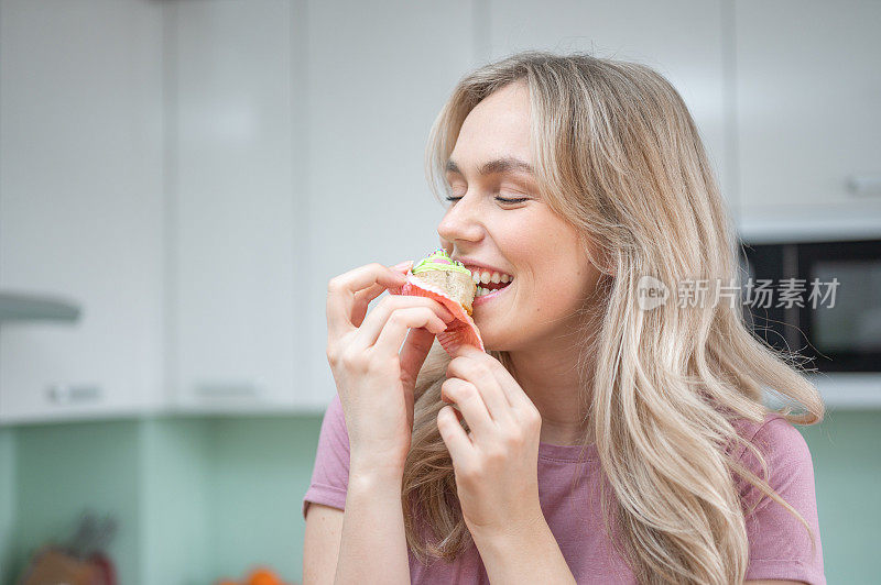 年轻女子微笑着，在厨房里咬着纸杯蛋糕