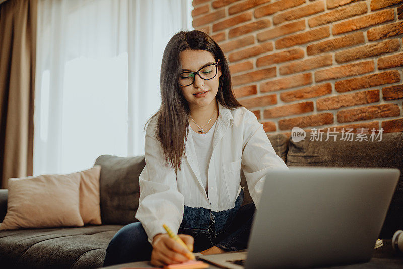 一位年轻的女学生坐在沙发上使用笔记本电脑耳机学习