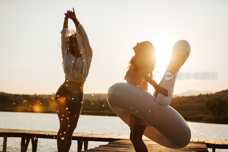 两个快乐的年轻女性朋友在湖上玩充气天鹅在日落