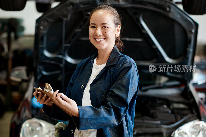 图为一名女机械师在汽车修理店工作时拿着剪贴板