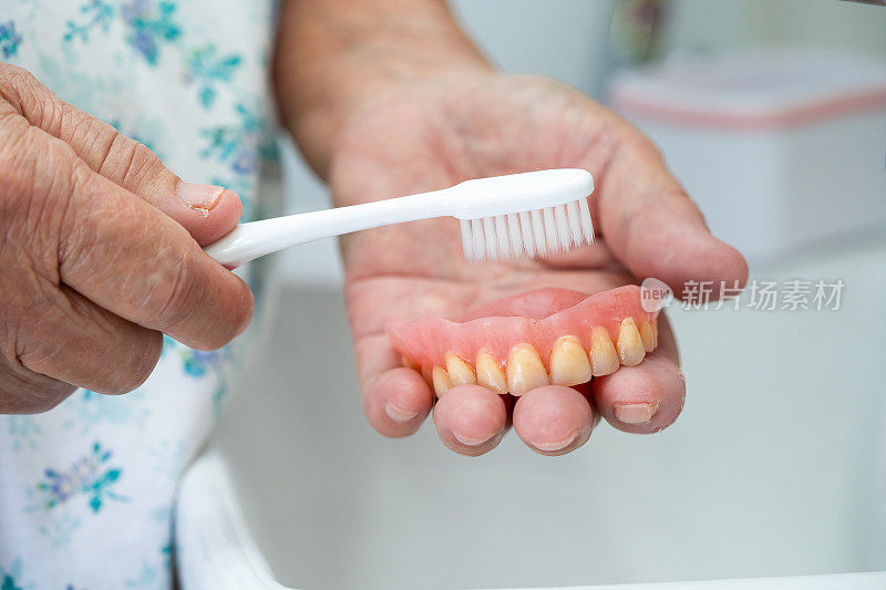 亚洲老年或老年妇女患者用牙刷清洁局部义齿替换牙。