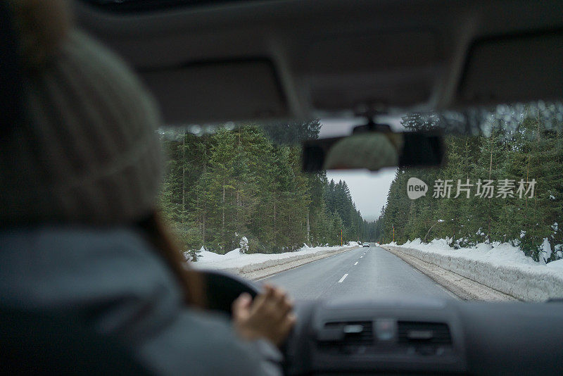 一名年轻女子开着车在雪原中穿过森林