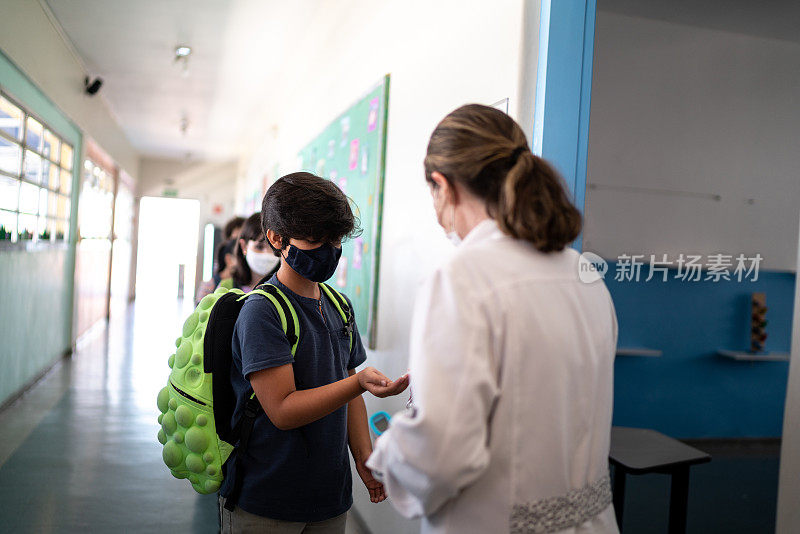 老师在学生进教室前，使用口罩在学生手上涂抹洗手液