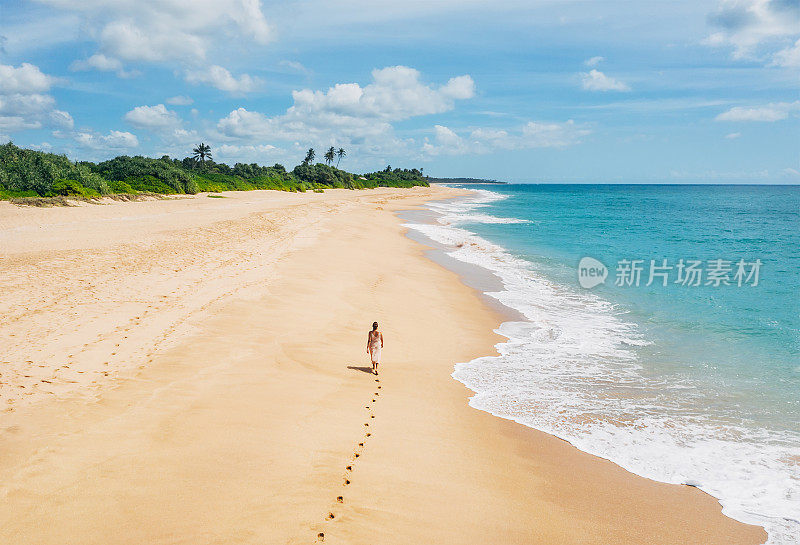 年轻的女性穿着轻夏装走赤脚在印度洋上留下脚印Tangalle孤独的椰子树海滩在斯里兰卡岛。俯视图无人机拍摄。