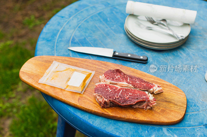 新鲜牛排。满足户外经验。晚餐在后院。木板上红肉。准备食物的过程。小牛肉。美味的小吃。户外餐