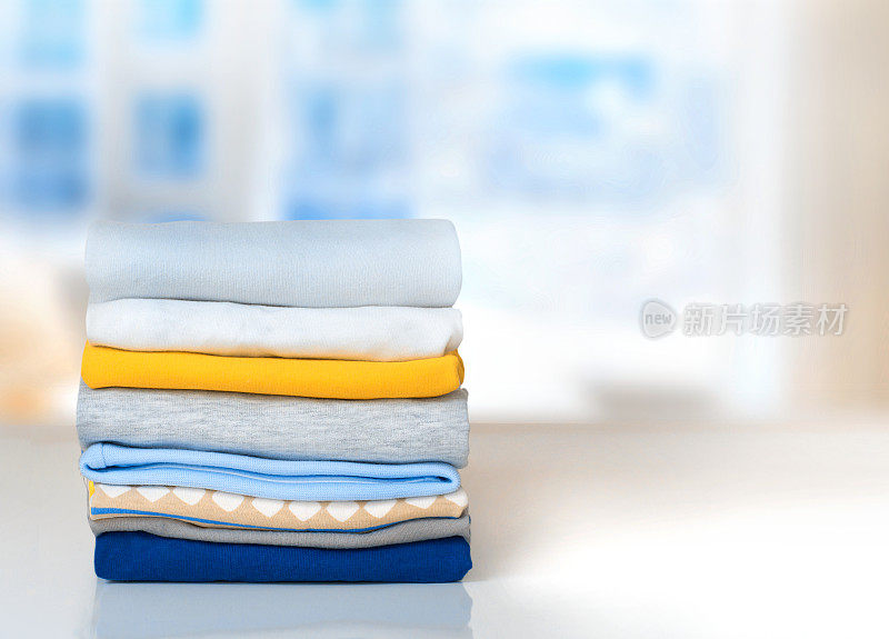 把折叠好的棉质衣服堆放在室内的桌子上。