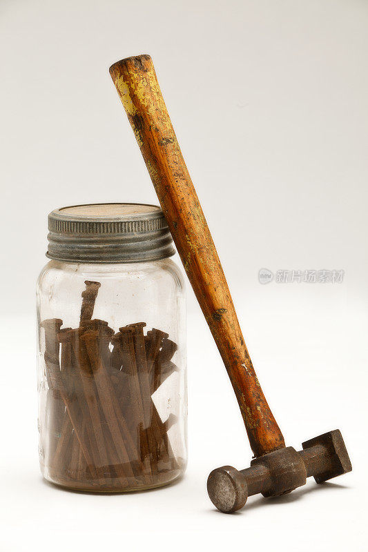 一把旧锤子倚在装满生锈铁钉的罐子上