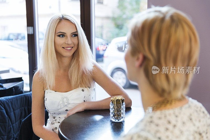 两个女孩坐在咖啡店的桌子旁，讨论着