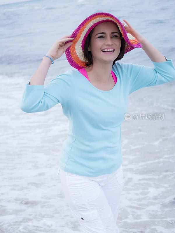 微笑的女性拿着帽子在海滩上