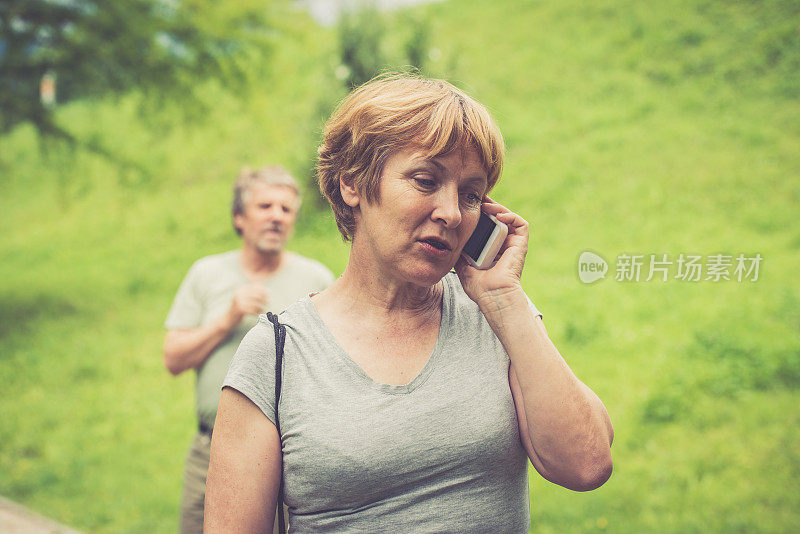 一对年长白人夫妇在户外，一个女人在用智能手机聊天