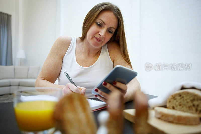 一个女人在早餐桌上用智能手机写笔记