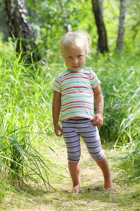 蹒跚学步的小女孩赤着脚走在森林里的小路上