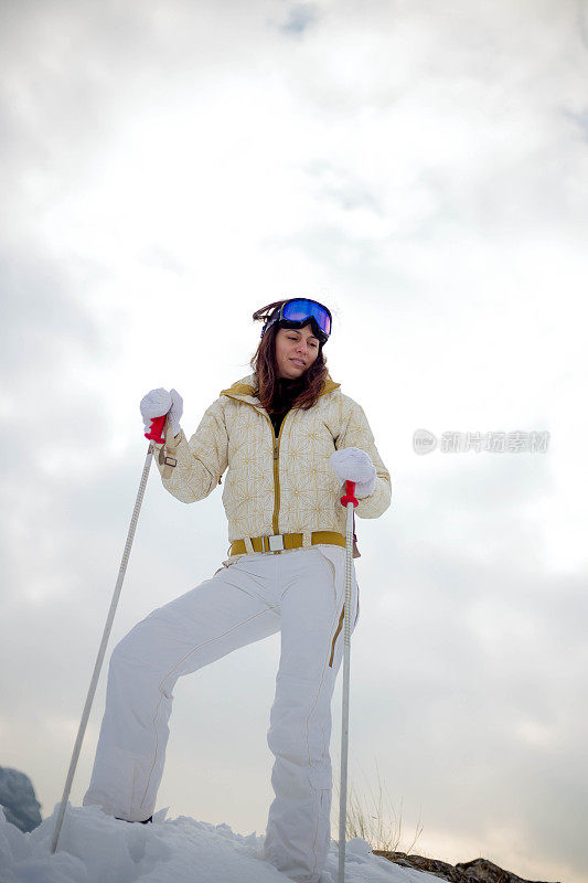 近景美丽的年轻女子在冬天的衣服站在一边，手拿木棍的背景雪山