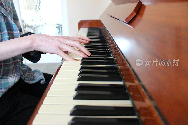 一个十几岁的男孩在弹钢琴，木制的钢琴键盘