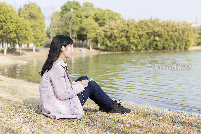 一个春天的下午，年轻女子戴着耳机在草坪上放松