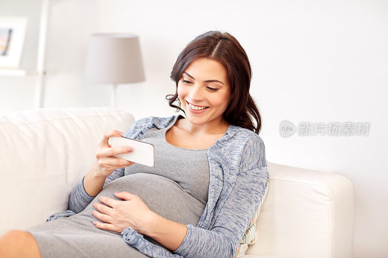 快乐的孕妇在家里用智能手机