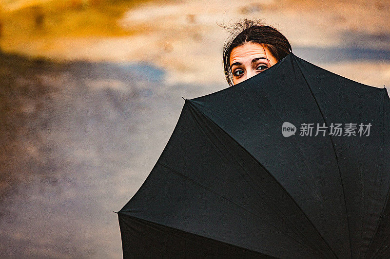 一个寒冷、刮风、下雨的秋日，一个年轻女子躲在雨伞后面站在户外。