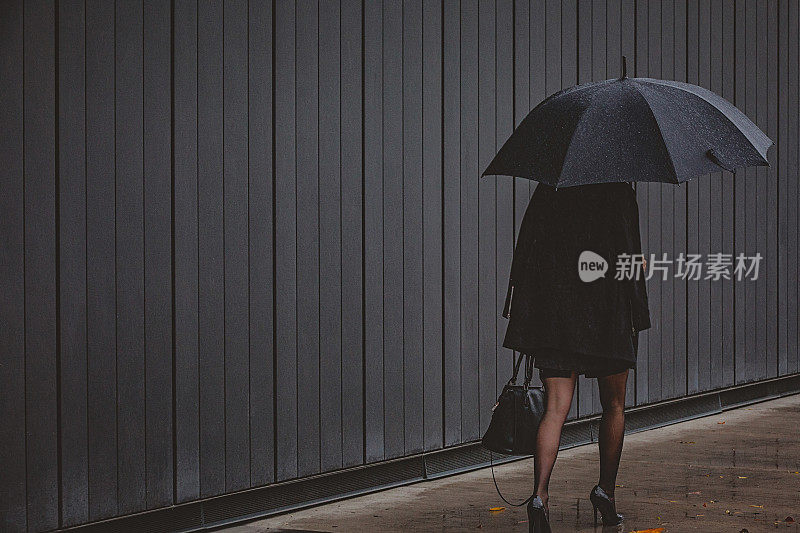 一名年轻女子撑着伞，在寒冷的秋日里在风雨中行走。