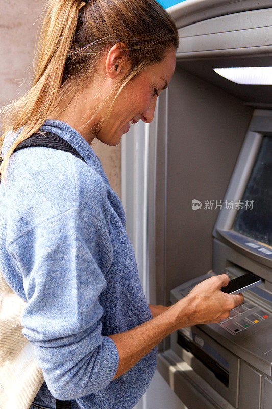 年轻女子用手机通过银行自动取款机