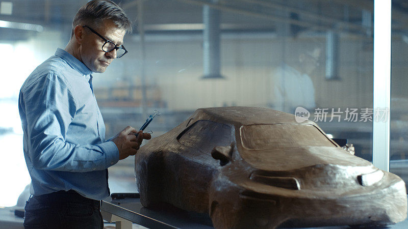 首席汽车设计师与Rake雕刻未来汽车模型从橡皮泥粘土。他在一家大型汽车厂的专门工作室工作。