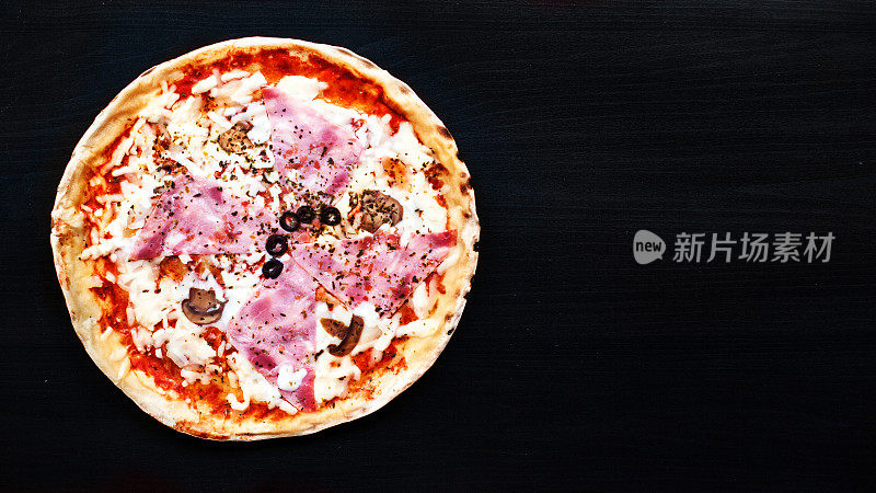 美味的肉披萨与火腿，辣香肠和培根在一个黑色的背景