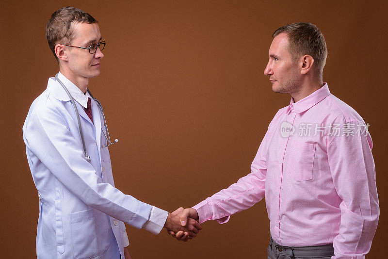 摄影室拍摄的年轻男子医生与男子病人在彩色背景下握手