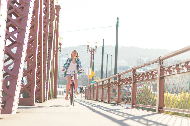 一个阳光明媚的下午，迷人的年轻女子沿着城市大桥骑自行车