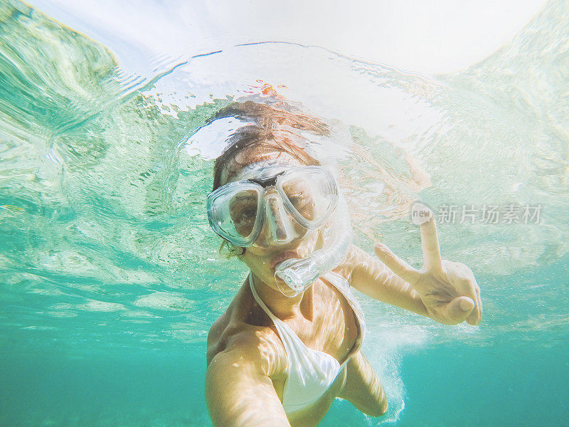 年轻女子在水晶蓝色的水下自拍，度假夏天的概念