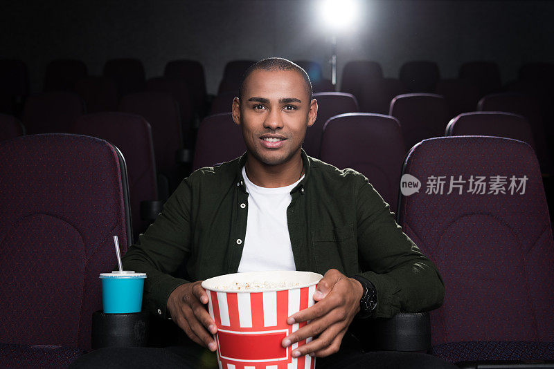 一个非裔美国人拿着爆米花和苏打水在电影院看电影
