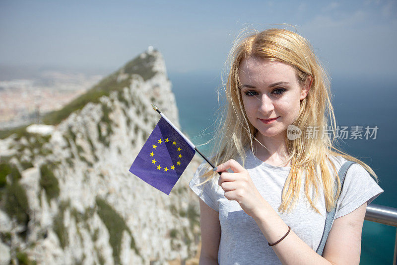 一名年轻女子举着一面欧盟旗帜，背景是直布罗陀岩石，表明了对其主权的争议和英国脱欧的影响