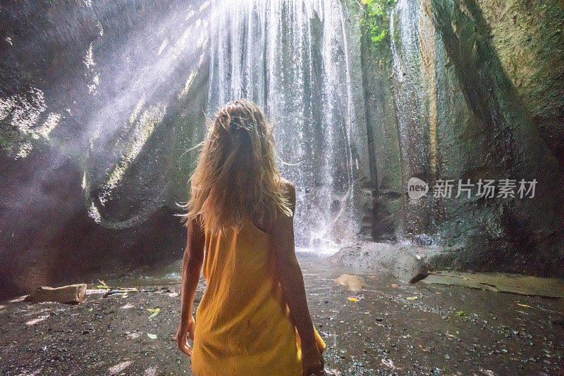 穿着黄色衣服的女孩站在热带雨林的洞穴里，仰望着从岩石上射下来的壮观的阳光。人们旅行的奇妙欲望自然的概念