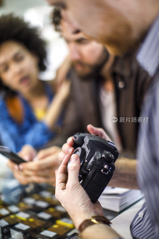 在一家相机店，卖家向几个买家解释单反相机的用法，其中一个买家正在使用手机