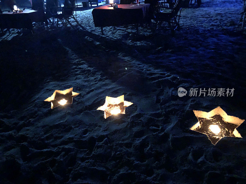 印度果阿海滨餐厅的餐桌上，在沙子上挖出一个星星形状的洞，夜晚的海滩蜡烛