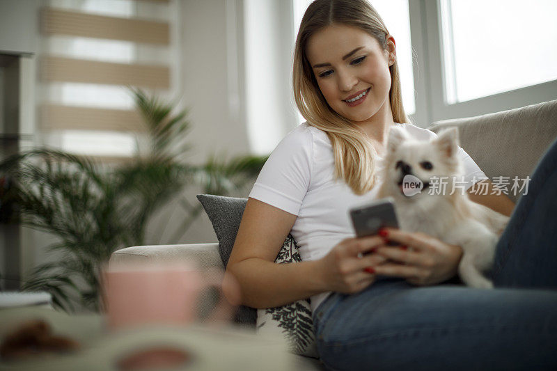 一个女人和她的狗在家里使用手机