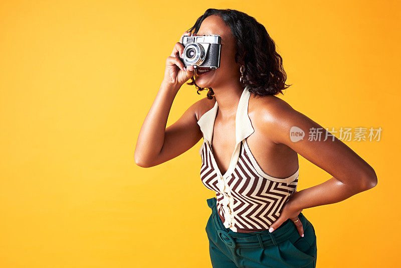 相机，摄影师和富有创造力的女人在摄影工作室的背景墙。快乐的黑人女孩和模特在黄色的背景下拍摄设计师时装的数码照片