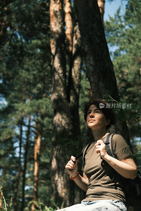 图为一名女背包客在森林中徒步旅行时在石头上休息