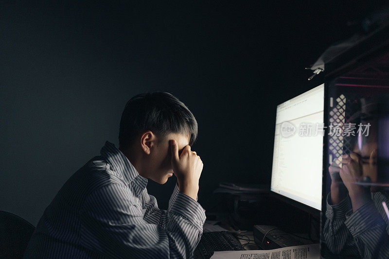 一名亚洲男子晚上在电脑前加班，感到眼睛很累——这是一种不健康的生活方式