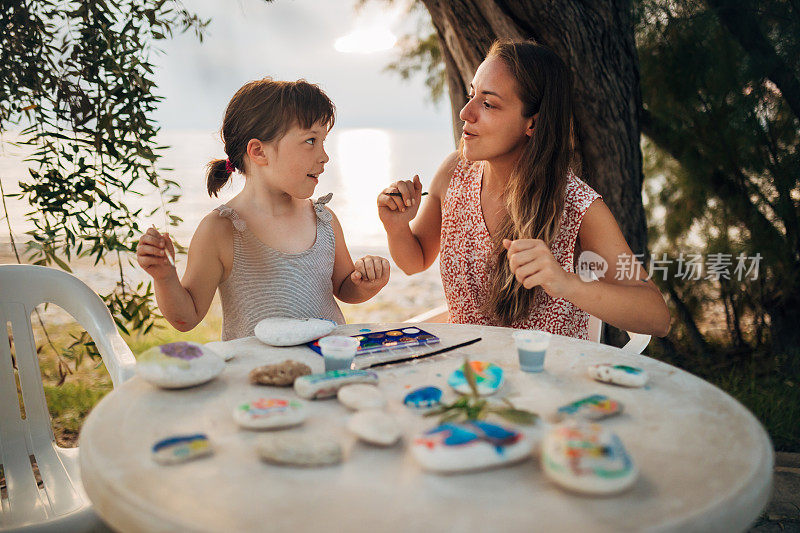 一个可爱的小女孩和她的妈妈跳舞，在岩石上画画，在离海滩不远的地方度过一天中最美好的时光