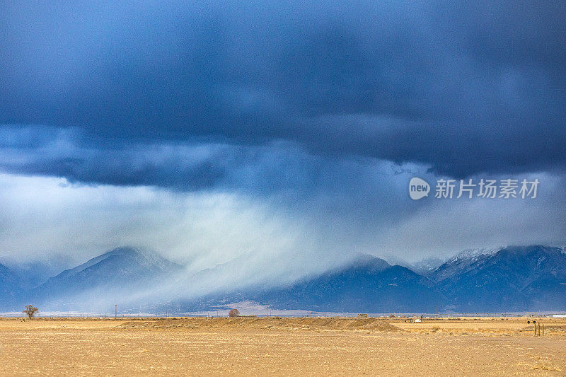 戏剧性的风暴云和雨在平坦的农田和雪山上移动