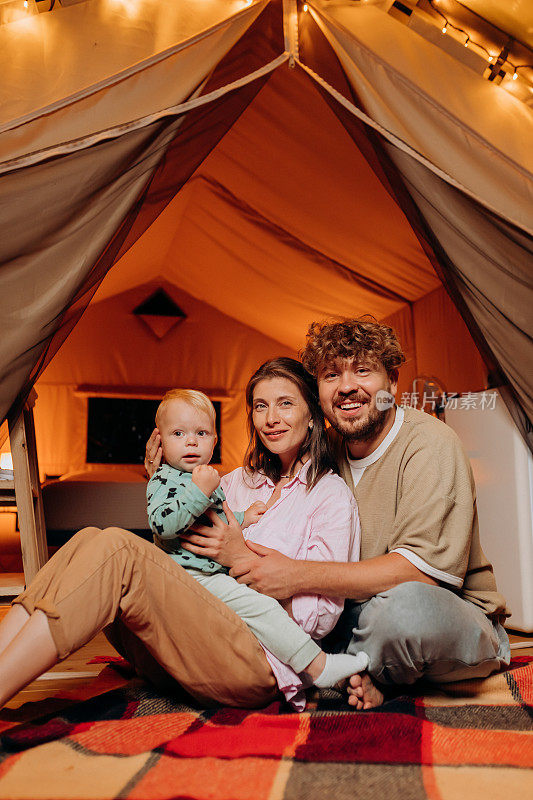 快乐的家庭和可爱的宝宝一起玩耍，在夏天的晚上一起露营。户外休闲休闲的豪华露营帐篷。生活方式的概念