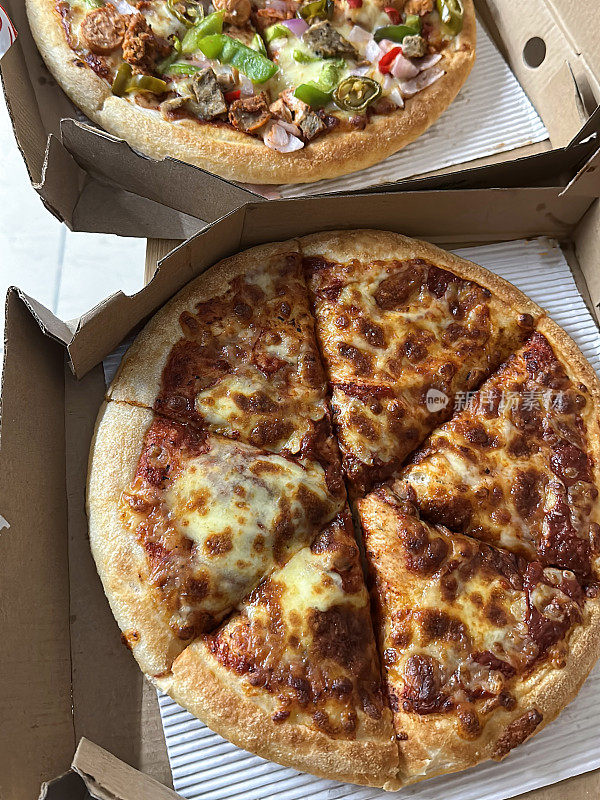 两个切片的披萨在硬纸板外卖披萨盒，玛格丽塔和肉盛宴披萨的特写图像，高架视图