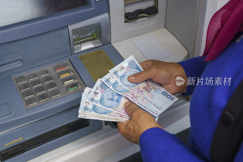 老妇人在自动取款机前拿着土耳其里拉钞票。取钱