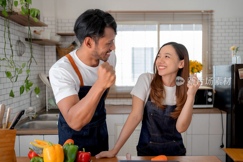 快乐的亚洲夫妇举起手臂庆祝成功完成在线烹饪课程