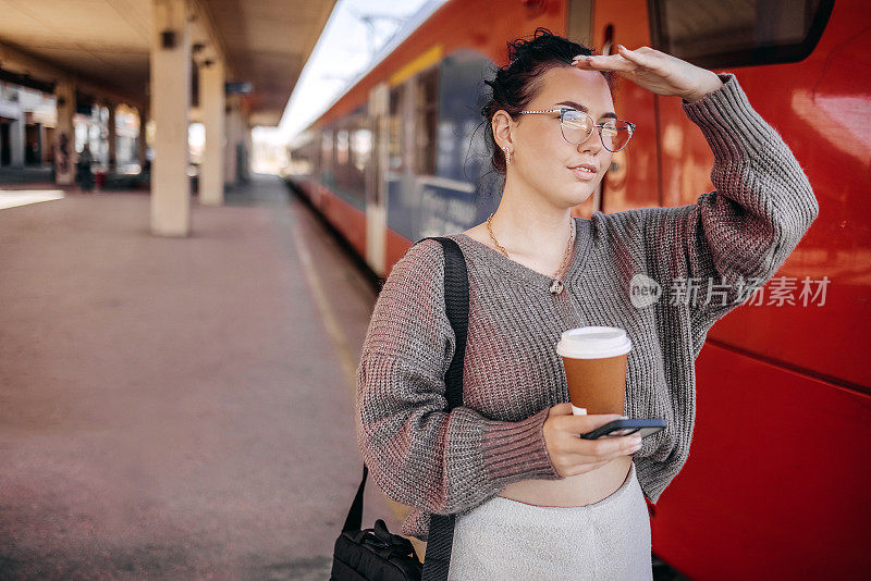 在上班路上等火车的年轻女子拿着一杯咖啡