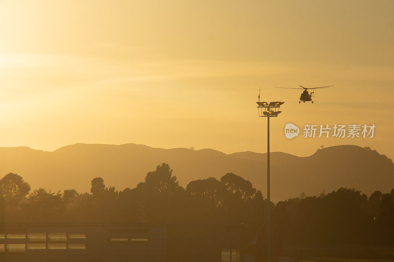 日落时分，一架直升机在城市上空盘旋，身后是群山和树木